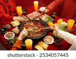 A lively hot pot gathering with various ingredients on a vibrant red table, featuring hands holding chopsticks and an array of colorful dishes.