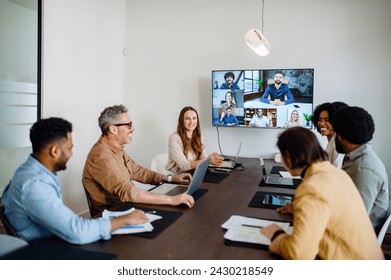 A lively and productive team meeting is captured where colleagues are connected via a large screen, showcasing a blend of in-person and remote collaboration. Virtual meeting concept - Powered by Shutterstock