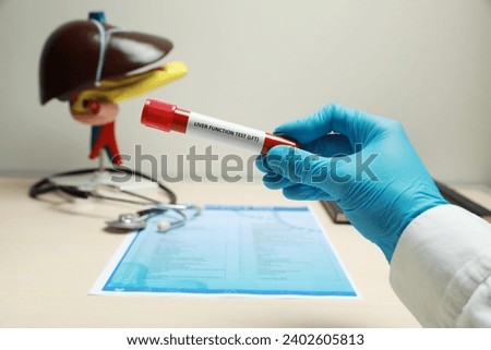 Liver Function Test. Laboratory worker with tube of blood sample, form and model of liver at table, closeup