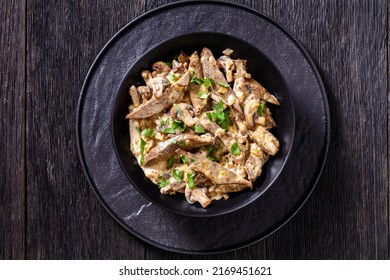 liver stroganoff with wholegrain mustard, onion and mushrooms in black bowl on dark wooden table with ingredients, horizontal view from above, flat lay, close-up