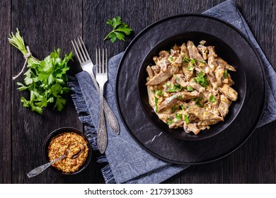liver stroganoff with wholegrain mustard, onion and mushrooms in black bowl on dark wooden table with ingredients, horizontal view from above, flat lay