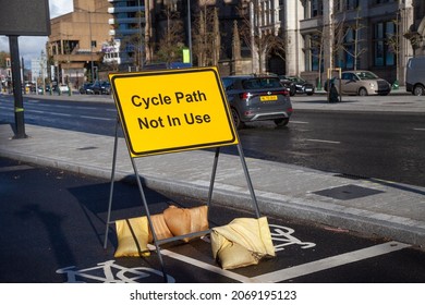 Liverpool, UK, November, 2021 - A Yellow Cycle Path Not In Use Sign, Situated On A Cycle Path Along The Side Of A Busy Road. Cars Are Passing, With Sandbags Holding Down The Sign. 