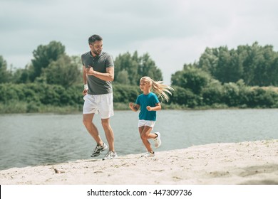 Living A Healthy Life. Full Length Of Cheerful Father And Daughter In Sports Clothes Jogging At The Riverbank Together 