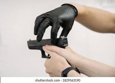 Living In A Pandemic. Shooting Instructor In  Gloves  Showing To The Client How To Use A Gun At A Shooting Range Amid A Pandemic