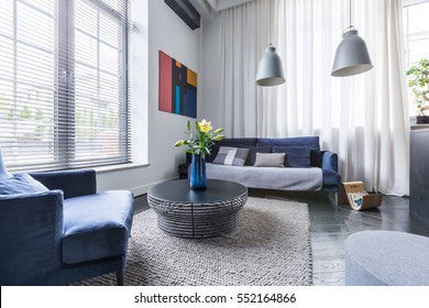 Living room with blue upholstered furniture, window blinds and white net curtain