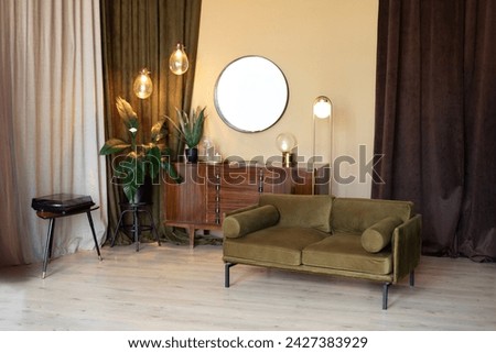 Living room with furniture. Retro Edison light bulbs. Mid century room in home with modern interior design, green velvet sofa, wooden cabinet, mirror, houseplants in pots and loft pendant lamps. 