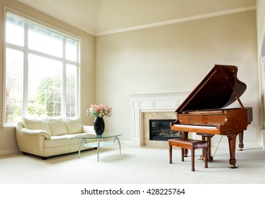 Living room with grand piano, fireplace, sofa and large window with bright daylight coming entering room. 