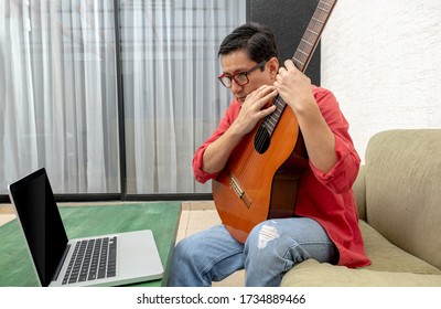 In The Living Room Of His House, A Man Looks Closely At His Computer Receiving A Virtual Guitar Lesson