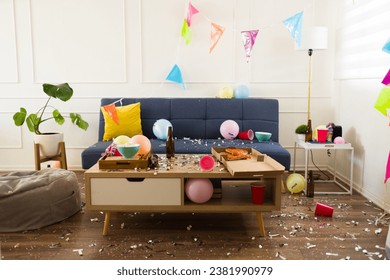 Living room home with confetti, balloons and party decorations having a disaster with trash and a mess after celebrating a birthday party 