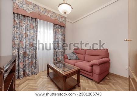 Living room of a house with a red fabric armchair, an interior table made of varnished wood and glass