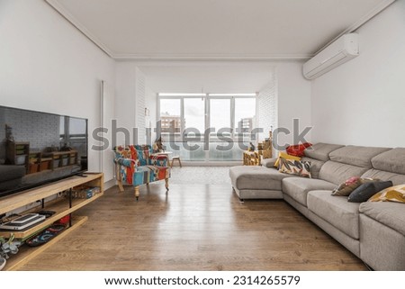 Living room of a house with a sofa upholstered in fabric with a chaise longue and on the wall in front of it a large TV on a wooden sideboard