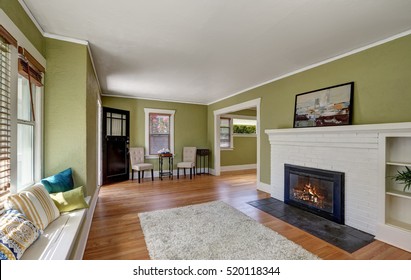 Living room interior design of craftsman home with white brick fireplace, built-in shelves, window seat with pillows, pale green walls and hardwood floor. Northwest, USA
