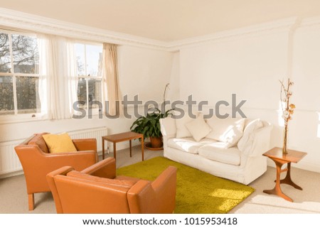Living room interior, enclosed in white walls and furnished with retro-styled leatherette armchairs, white couch, and green rug.