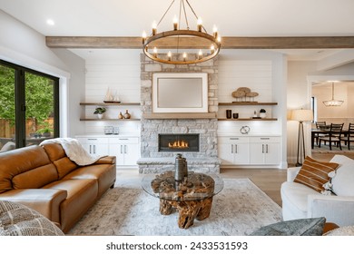 Living room interior with exposed wooden beams on the ceiling carmel colored leather sofa round wagon wheel chandelier fluffy white throw blanket hardwood floor view to kitchen and stone fireplace - Powered by Shutterstock