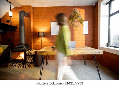 Living Room Interior In Loft Style With Wooden Table And Burning Fireplace At Home. Motion Blurred Person Passing By