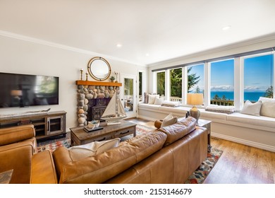 Living room with large windows ocean view river rock fireplace chestnut color leather sofa and chairs pool table