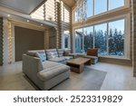 Living room in a luxurious wooden house with an exclusive chandelier on a high ceiling. The panoramic window lets in the rays of the winter sun.