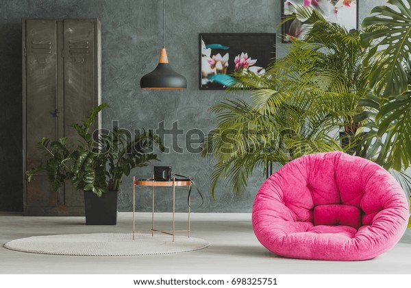 Living room with pink plush armchair, exotic\
plants and retro camera on metal\
table