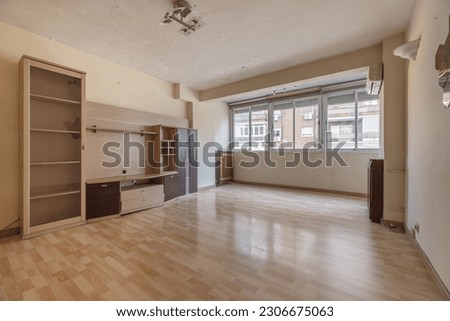 A living room with a wall with some loose furniture, cheap wooden floors and a large window with aluminum windows