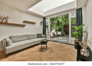 a living room with wood flooring and skylight above the couch is in front of an open glass door