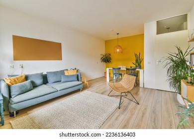 a living room with wood flooring and yellow accent wall behind the sofa is a blue couch that sits on a white area rug
