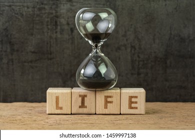 Living time for human life countdown, lifetime or retirement concept, sandglass or hourglass on wooden cube block with alphabet building the word Life on wood table, dark black background.