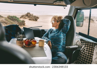 Living and working inside camper van vehicle in travel and digital nomad free lifestyle. One woman sitting in a motorhome and enjoy relax and laptop connection. Beach in background outside the window