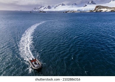 Livingston Island, Antarctica - 12 05 17: Elevated view of an inflatable zodiac boat and boat wake with expedition tour guide driving across waves and a scenic view of Antarctic mountains and glaciers