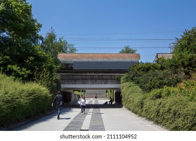 LJUBLJANA, SLOVENIA - JUNE 17, 2021: People Walking On A Pedestrain Path Passing Under A Railway Bridge With A Freight Train Above In Tivoli Park.Tivoli Park Is Main City Garden Of Slovenian Capital