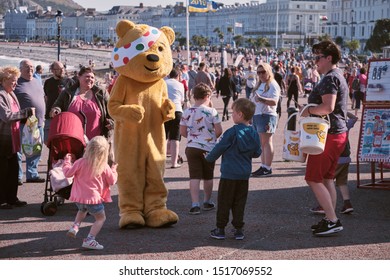 Llandudno, Wales, September 21, 2019. 
 Young Kids Surrounding Pudsey Bear, BBC Children In Need's Mascot With Esplanade In Llandudno In Background On Sunny Autumn Day.