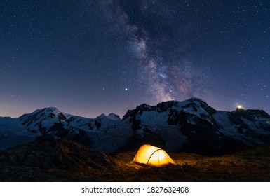 lluminated red tent high in the mountains under the night sky with the milkyway.