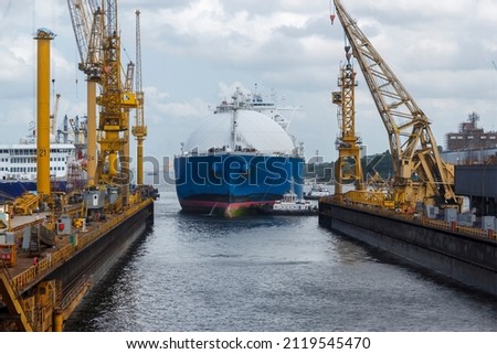 LNG carrier arriving to a ship repair yard assisted by multiple tugboats. Floating dock is submerged to allow the vessel in.