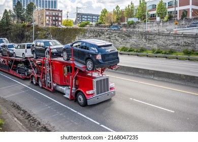 Loaded big rig industrial red car hauler semi truck tractor transporting vehicles on the modular hydraulic semi trailer running on the highway road at the city limit going to point of destination