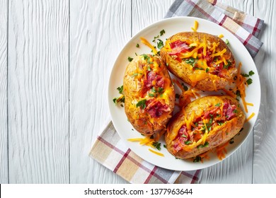 Loaded freshly Baked hot Potatoes with crispy fried Bacon, pulled chicken breast and melted cheddar cheese on a white platter on a wooden table, view from above