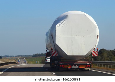 Loaded Lowbed Semi Truck With Big Barrel Tented Construction Move On Suburban Asphalt Road, Rear View On Blue Sky Background, Oversized Transport Logistics