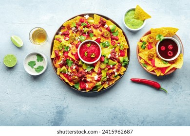 Loaded nachos. Mexican nacho chips with beef, overhead flat lay shot with guacamole sauce, cheese salsa, tequila drinks, limes, with a place for text - Powered by Shutterstock