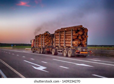 A loaded timber truck transports timber logs with an overload on the highway, black smoke. The concept of transportation of timber and wood, copy space, business