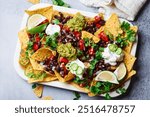 Loaded vegan nachos with guacamole, black beans and salsa for party, top view.