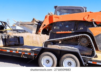 Loader with attachments is positioned on trailer by construction site along road