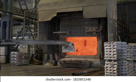 Loader mixing red-hot aluminium in bowl in aluminium plant. Aluminium foundry furnace loaded with metal. Red hot flames glowing and liquid melting. Fire melts aluminum ingots in a blast furnace.