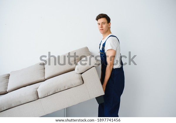 Loader moves sofa, couch.
worker in overalls lifts up sofa, white background. Delivery
service concept. Courier delivers furniture in case of move out,
relocation.