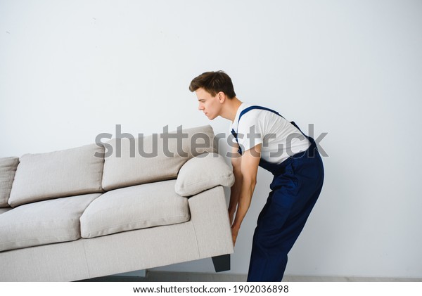 Loader moves sofa, couch.\
worker in overalls lifts up sofa, white background. Delivery\
service concept. Courier delivers furniture in case of move out,\
relocation.