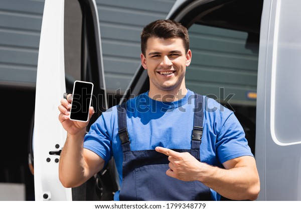 Loader pointing with finger at smartphone with\
blank screen near truck\
outdoors