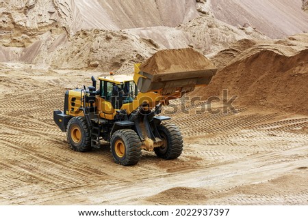 The loader works in a sand quarry. A yellow front loader moves gravel in a bucket. Close-up.