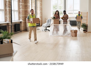 Loaders In Vests Carrying Moving Boxes In Office While Multi-ethnic Employees Setting Up New Space