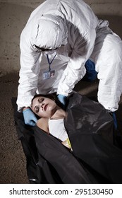 Loading Body Bag With Addicted Woman On Crime Scene