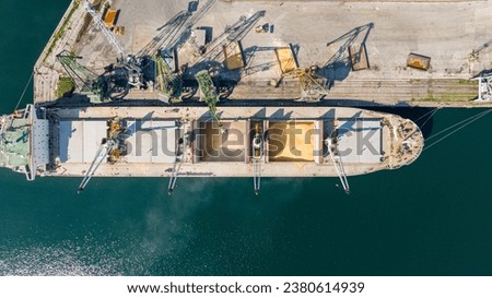 Loading dry cargo ship of wheat by cranes in port. Top down view loading into holds of sea cargo vessel
