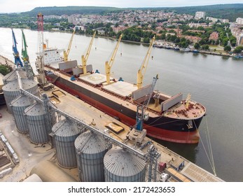 Loading grain into holds of sea cargo vessel in seaport from silos of grain storage. Bunkering of dry cargo ship with grain. Aerial top view - Shutterstock ID 2172423653