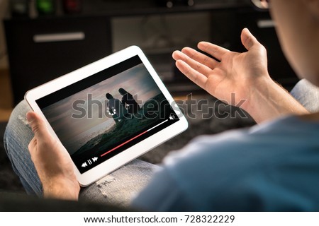 Loading icon rolling on video in an online movie streaming service. Bad and slow internet connection. Film player stopped. Frustrated and confused man watching and holding tablet while spreading arms.