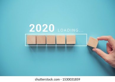 Loading new year 2020 with hand putting wood cube in progress bar.